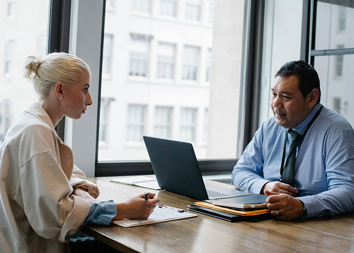 Two professionals in an interview setting, discussing over a laptop, capturing an awkward job interview moment.