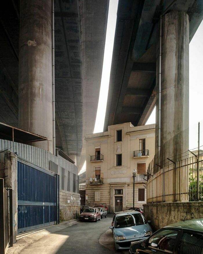 Urban hell scene with cars parked under an overpass beside an old building, illustrating urban decay.