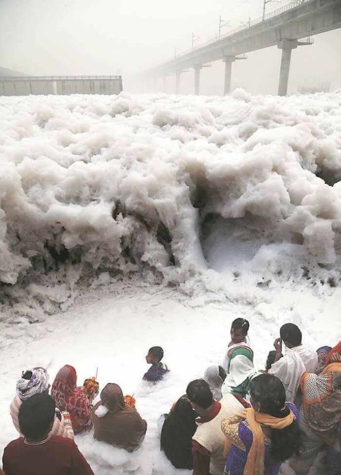 Urban hell scene with people standing in thick foam pollution near a bridge.