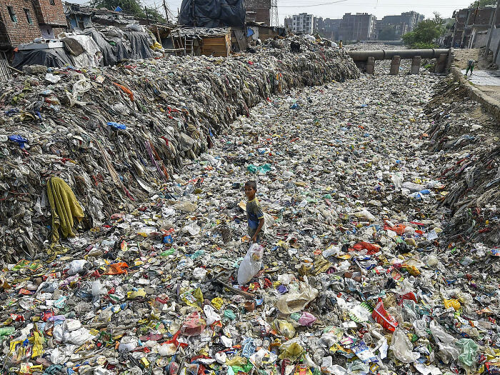 A child standing in a garbage-filled urban hell, surrounded by piles of waste in a polluted area.