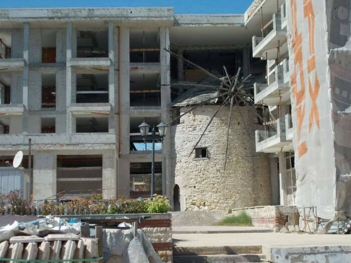 Abandoned urban hellscape showing dilapidated buildings and a crumbling windmill in a modern city setting.