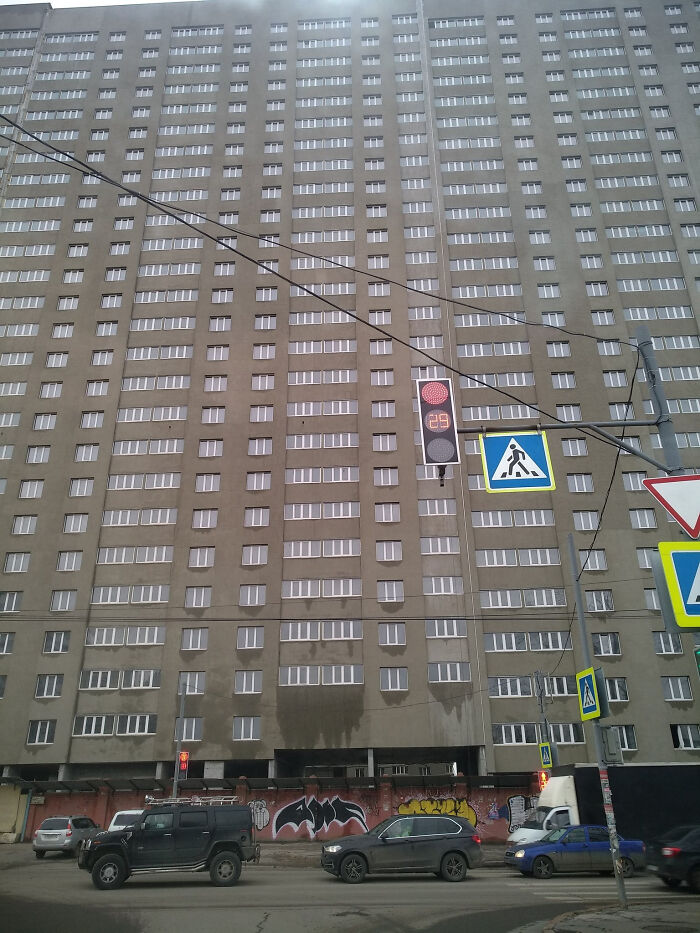 Urban hell: Tall, bleak apartment building with graffiti-covered ground level, surrounded by cars and traffic signs.