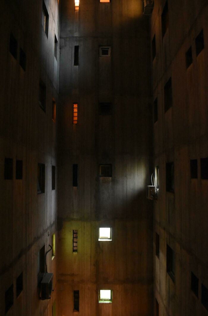 Inside a dark, windowless urban hell, dim lights illuminate the stark concrete walls, conveying a haunting atmosphere.