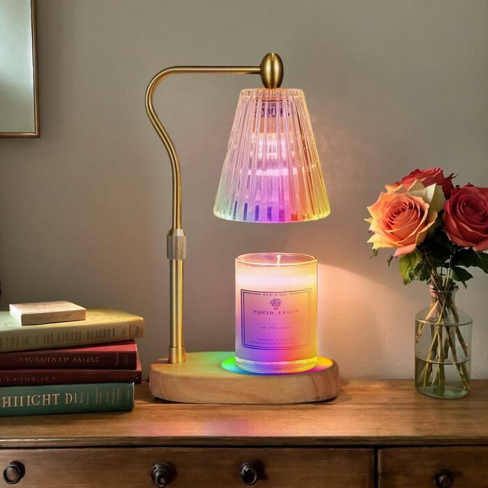 Cozy products: a warm desk lamp illuminating a candle and books with roses in a vase nearby.