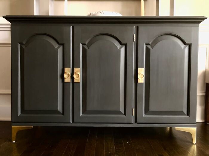 Modern dark cabinet with gold handles and legs, enhancing contemporary apartment decor.