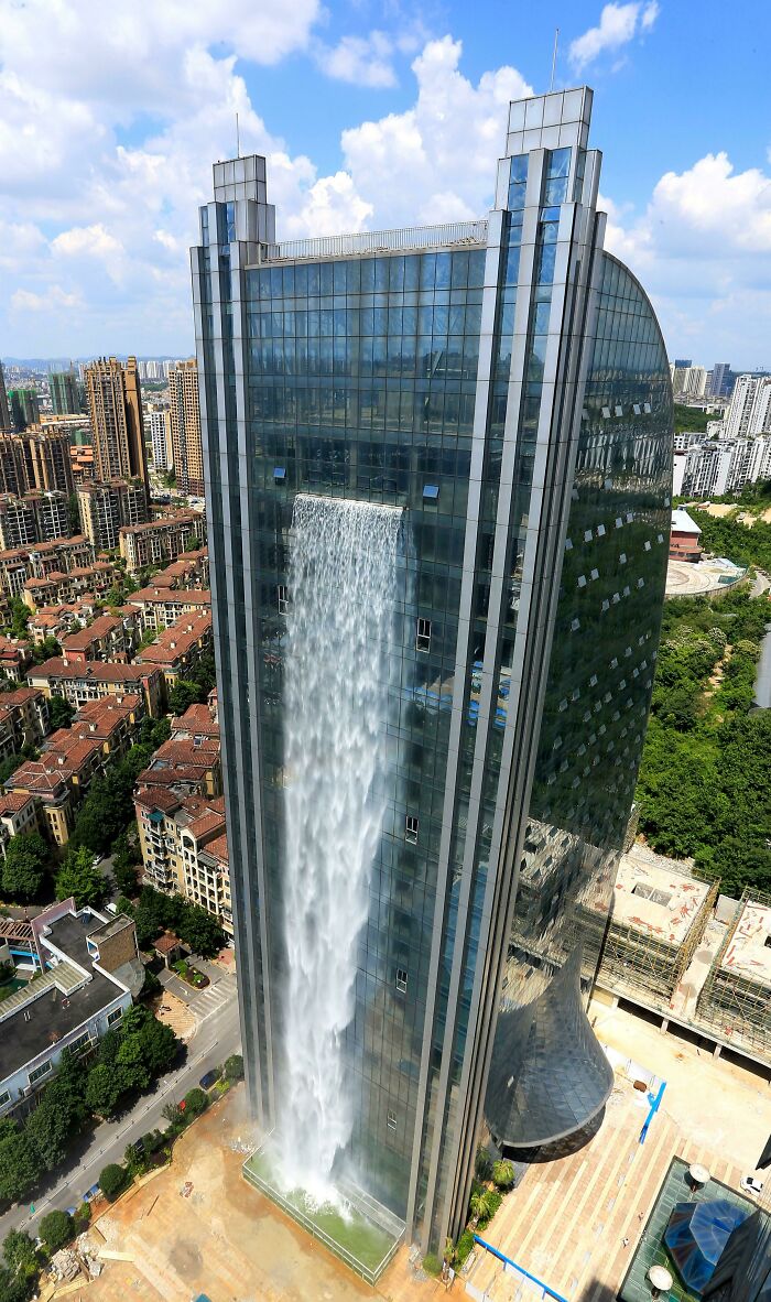 A skyscraper with a massive urban waterfall cascading down its facade, surrounded by city buildings.