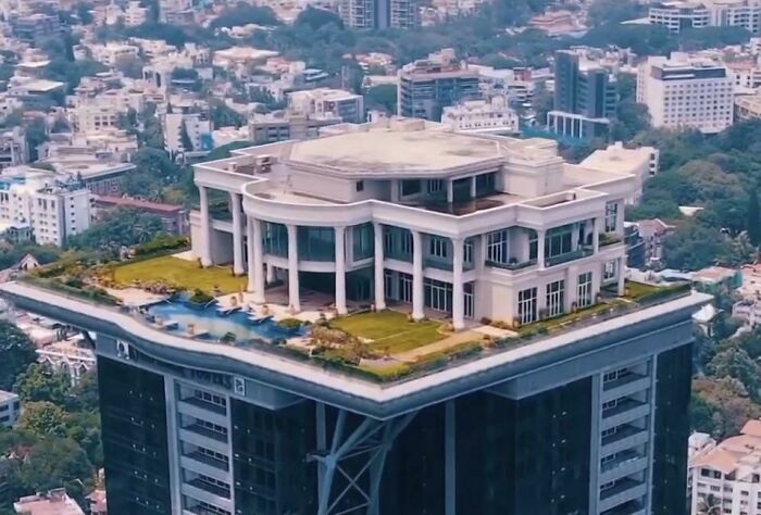 Rooftop mansion on high-rise building in urban hell, surrounded by dense cityscape.