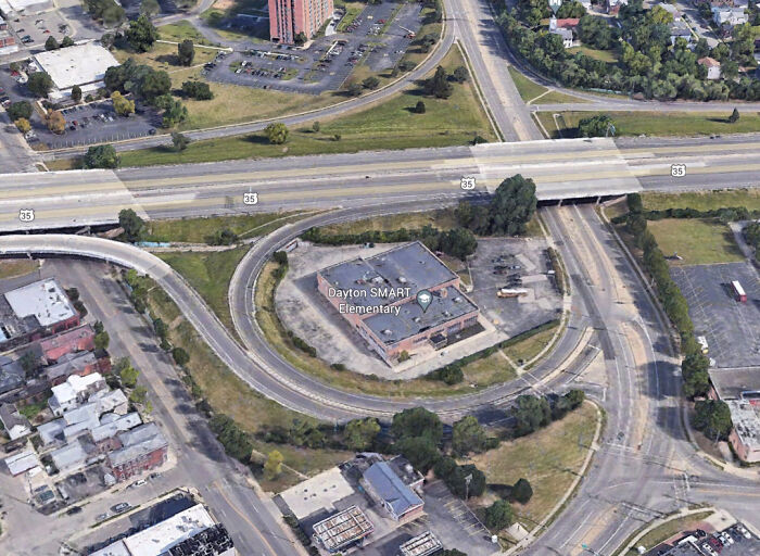 Aerial view of an urban setting with highways encircling a school building, illustrating urban hell design.