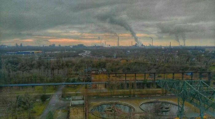 Urban landscape with smoky industrial skyline, overcast sky, and winding roads depicting urban hell scenario.