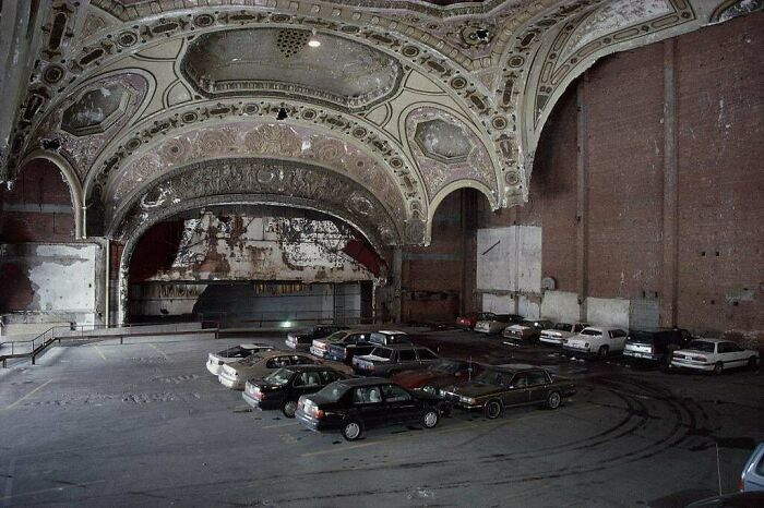 Urban hell: an abandoned theater repurposed as a parking lot, with ornate ceilings contrasting the bleak scene below.