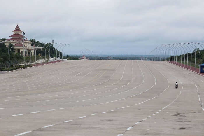 Desolate urban scene featuring an empty, wide boulevard and a lone scooter under a cloudy sky, illustrating urban hell.