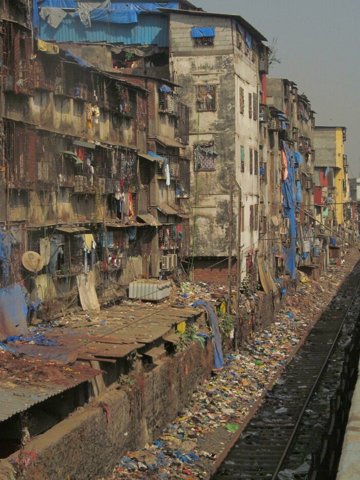 Urban hell scene with deteriorating buildings and garbage-strewn railway, depicting harsh living conditions.