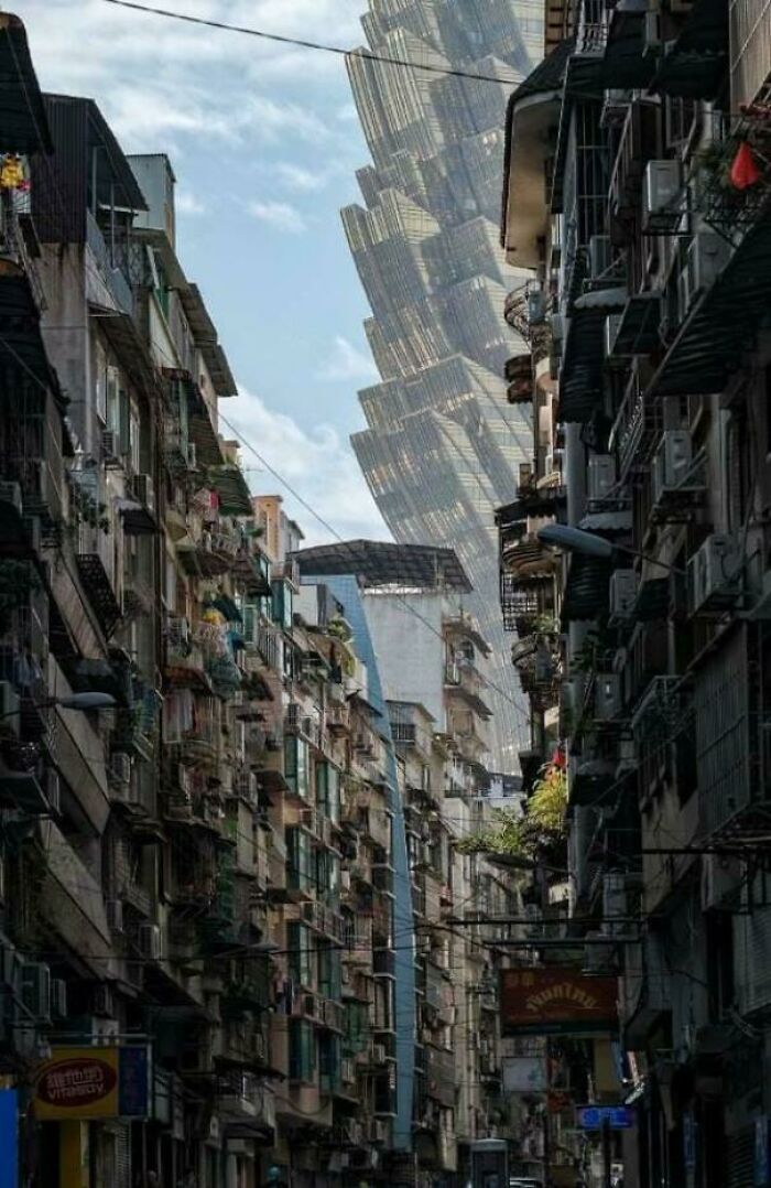 Tall futuristic skyscraper looms over crowded, decaying urban neighborhood, depicting an urban hell scenario.