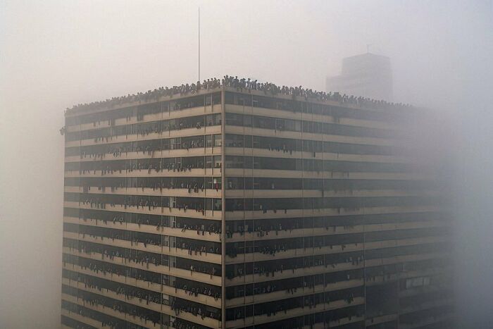 Foggy cityscape with a crowded rooftop, illustrating symphonic chaos of modernity.