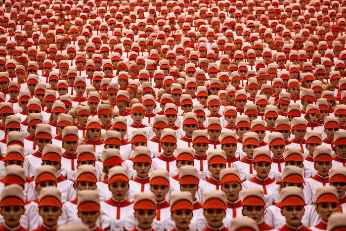 A sea of people in synchronized formation, dressed in red and white, illustrating the symphonic chaos of modernity.