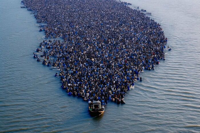 Massive crowd forms a dense, chaotic shape in water, symbolizing the symphonic chaos of modernity.