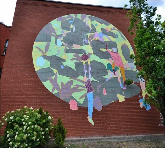 Colorful mural by a Montréal artist on a brick wall, featuring abstract figures and foliage, transforming a dull space.