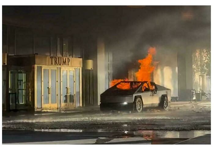 A futuristic car in flames outside a building, suggesting a boring dystopia.