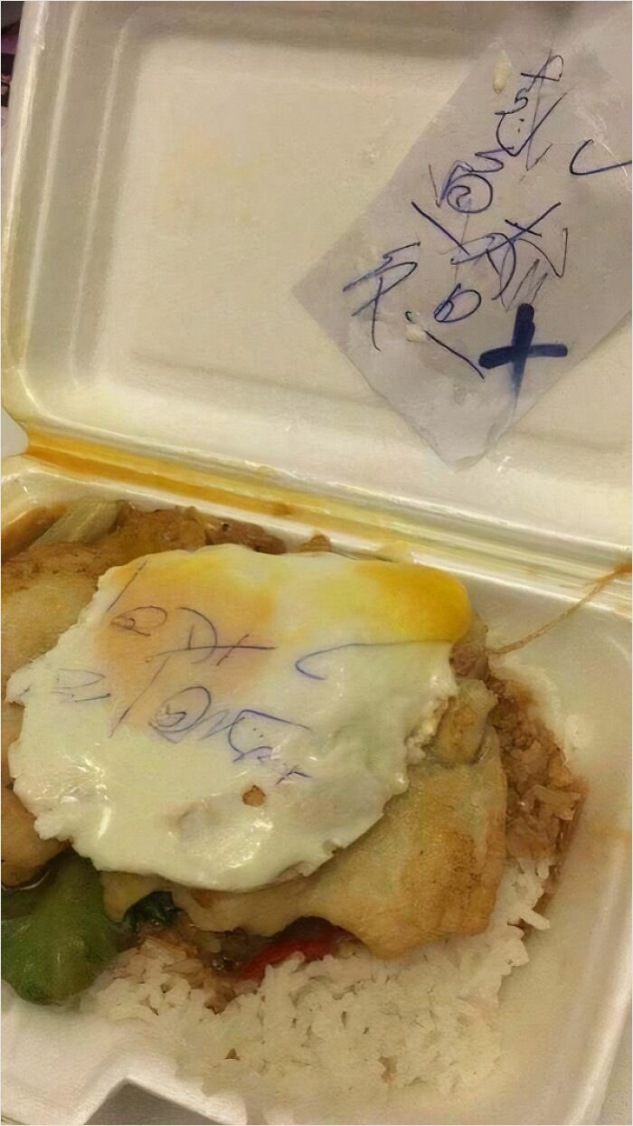 Unusual food with writing on an egg atop rice in a styrofoam container.