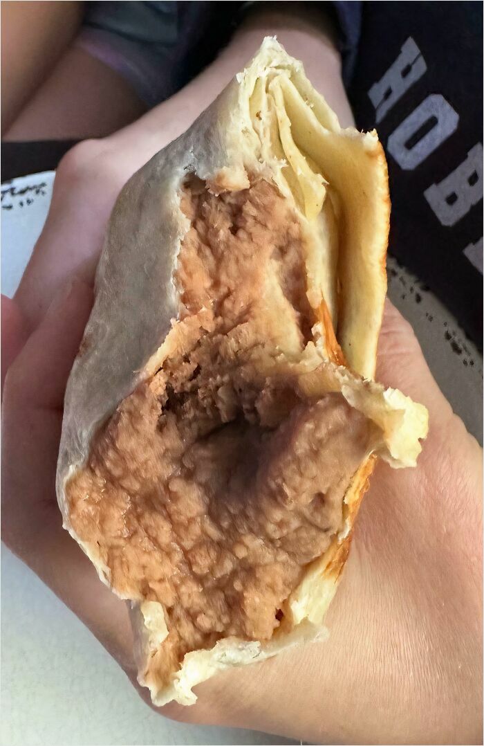 Unhinged food: close-up of a bean burrito held in hand, showcasing its unusual filling texture.