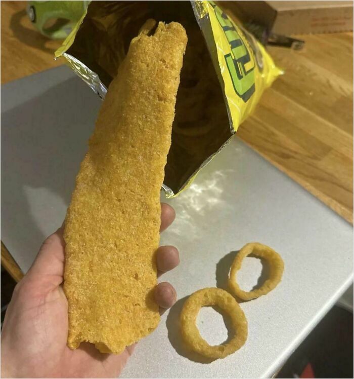 A large chip alongside two onion rings on a table, demonstrating absolute-units-things in snack sizes.