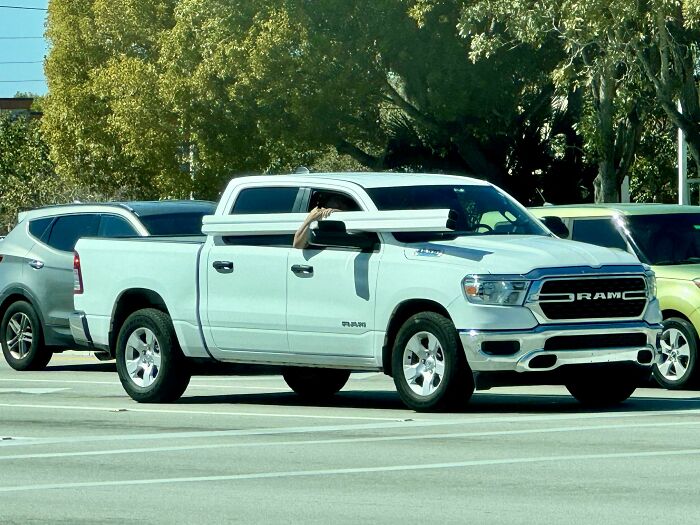 Large white truck in traffic with an unsecured long beam, highlighting unsafe driving behavior in cars.