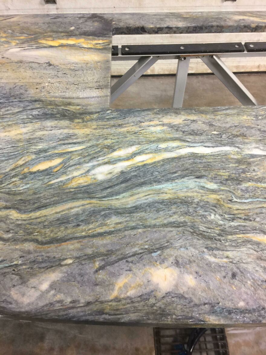 Marble countertop with swirling patterns resembling abstract art, featuring shades of gray and hints of yellow.