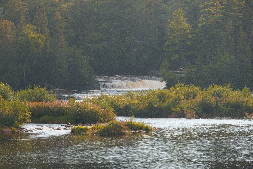 Scenic waterfall view surrounded by lush greenery and a serene river, resembling an accidental art composition.