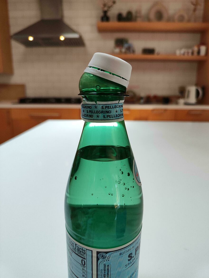 A green glass bottle of sparkling water with a tilted cap, showcasing accidental art in a kitchen setting.