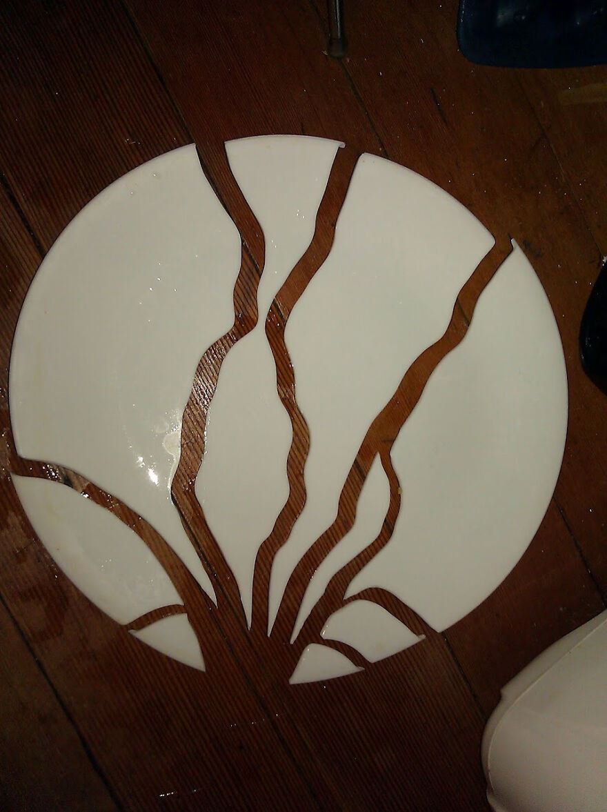 Cracked round plate forming tree-like pattern on wooden floor, an example of accidental art.