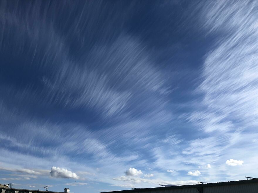 Abstract cloud patterns in the sky resembling accidental art above rooftop silhouettes.