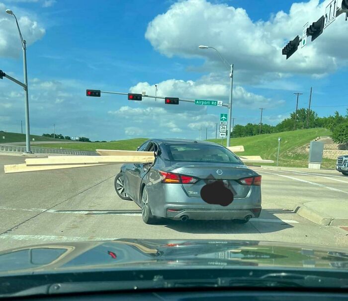 Car carrying oversized wood load, poorly secured, extends dangerously from windows, under traffic lights.