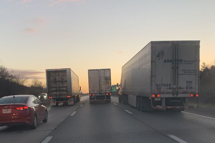 Three trucks blocking highway lanes at sunset, with a red car in the left lane, highlighting road chaos and traffic idiocy.