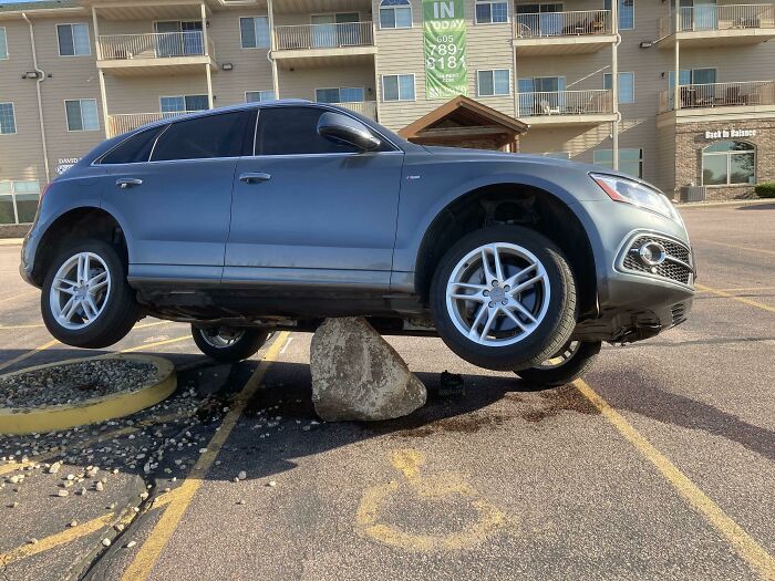 Car stuck on a rock in a parking lot, illustrating a common "Idiots in Cars" scenario.