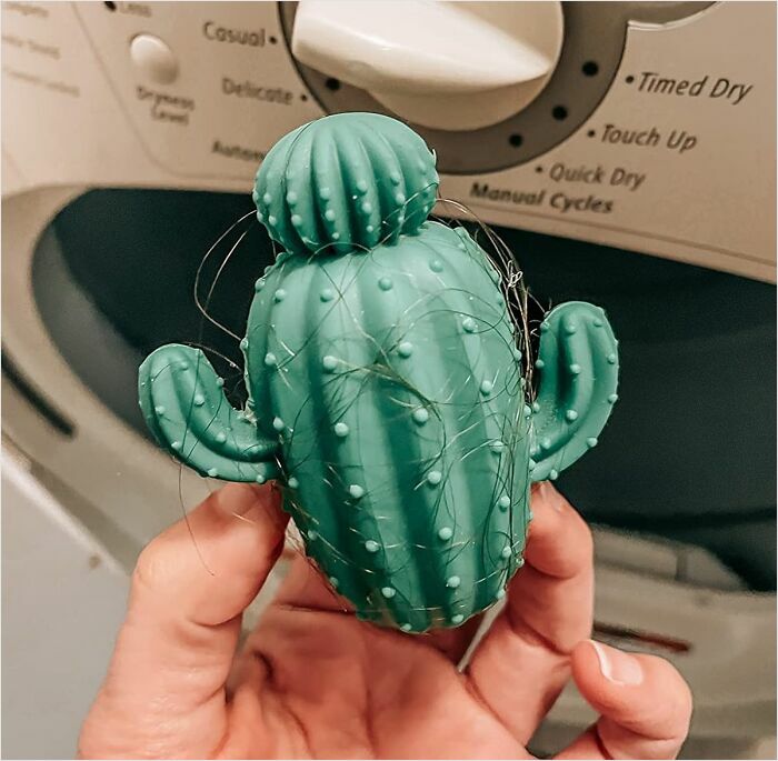 A quirky cactus-shaped dryer ball held in front of a washing machine, adding fun and functionality to laundry tasks.