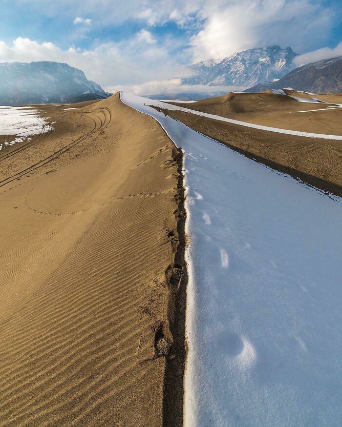 Incredible world photo of a desert landscape with a snow-covered path, leading towards distant mountains under a blue sky.