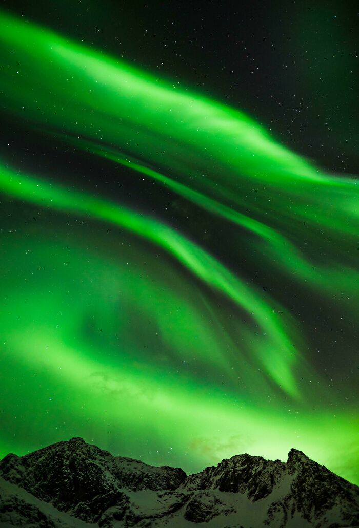 Aurora borealis glowing over snow-covered mountains, showcasing incredible world photos.