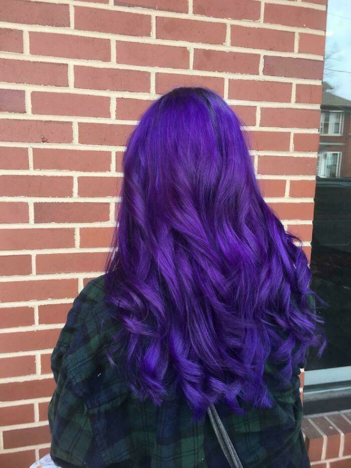 Person with vibrant purple hair standing against a brick wall, showcasing changing hair color.