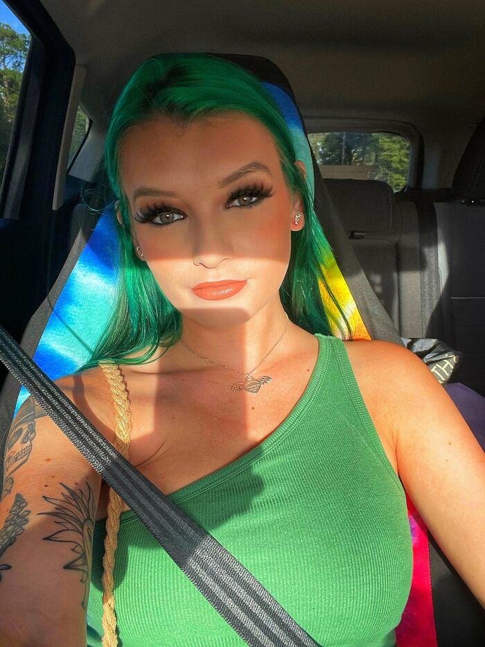 Woman with green hair in a car, showcasing changing hair color and wearing a green top, sunlight casting shadows.