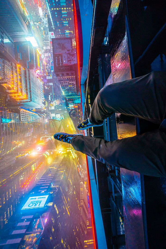 Feet dangling from a rooftop, showcasing an incredible world view of a vibrant cityscape below at night.