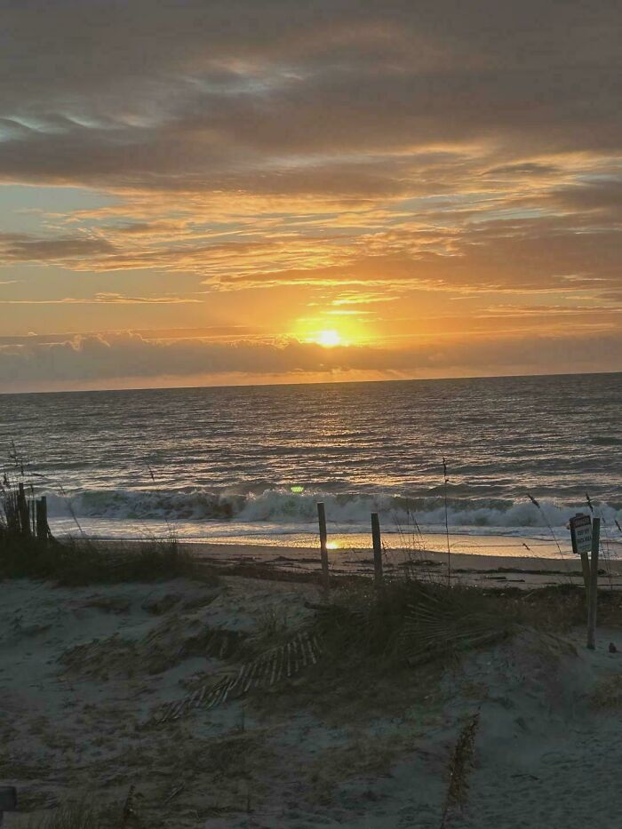 Sunset over ocean waves with a sandy beach in the foreground, capturing an incredible world photo scene.