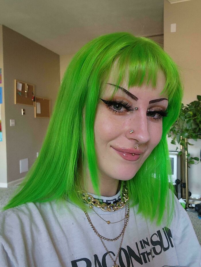 Person with vibrant green hair and piercings showcasing a changing-hair-color style indoors.