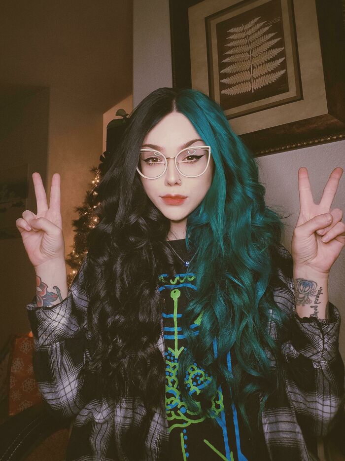 Person with glasses and dual-tone hair in black and teal, making peace signs, showcasing changing hair color.