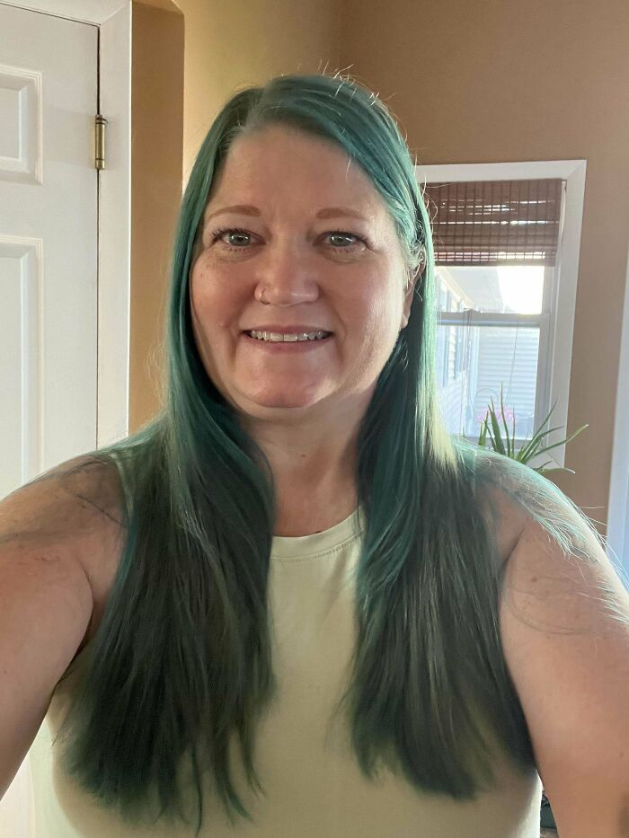 Person with long, teal-colored hair, smiling indoors, highlighting a changing hair color trend.