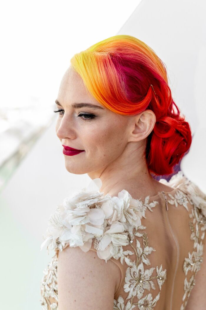 Woman with vibrant changing hair color in red, orange, and yellow hues, wearing an elegant floral dress.