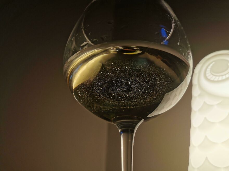 A wine glass creating an accidental-art effect with swirling liquid, resembling a galaxy against a soft light background.