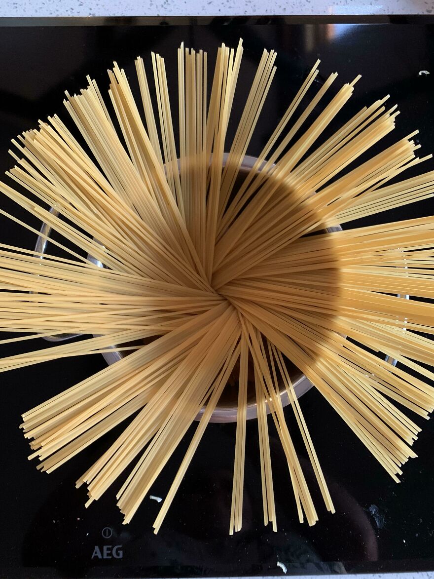 A pot of uncooked spaghetti arranged in a starburst pattern, showcasing accidental art on a stovetop.