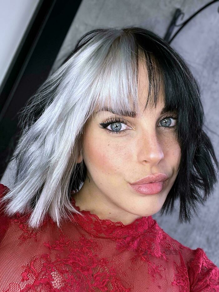 Woman with a striking black and white hairstyle, showcasing changing hair color, in a vibrant red lace top.