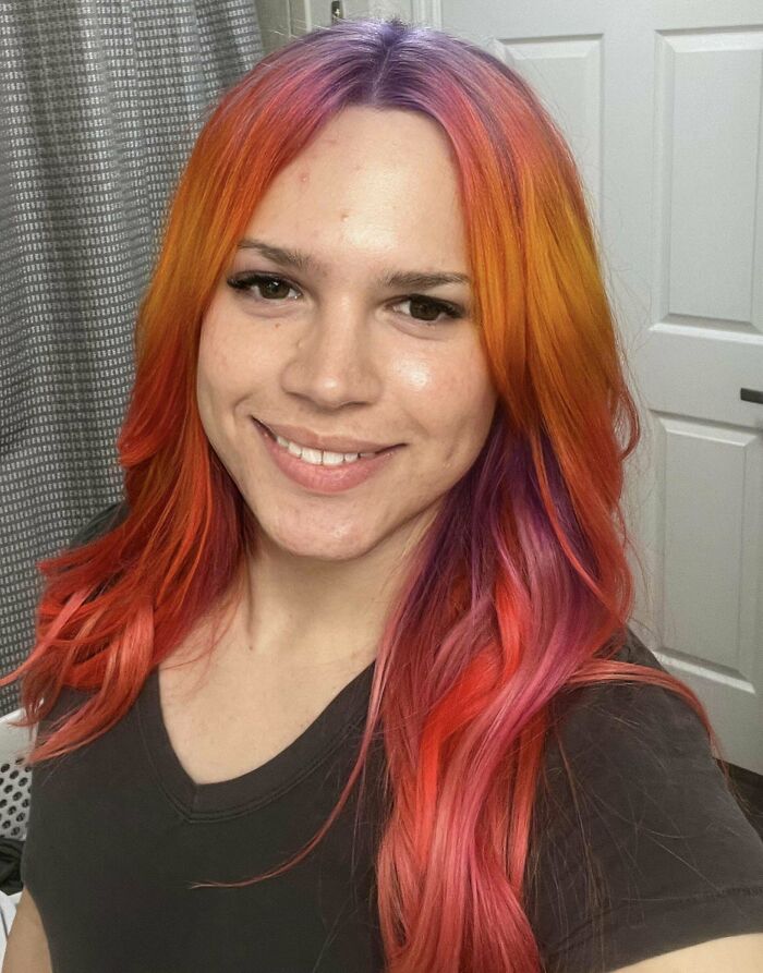 Person with vibrant changing-hair-color in a bathroom, featuring orange, pink, and purple hues.