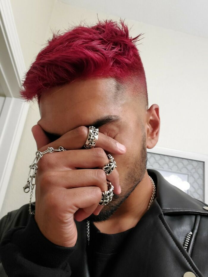 Person with vibrant red hair covering face, showcasing changing hair color, wearing silver rings and a black jacket.